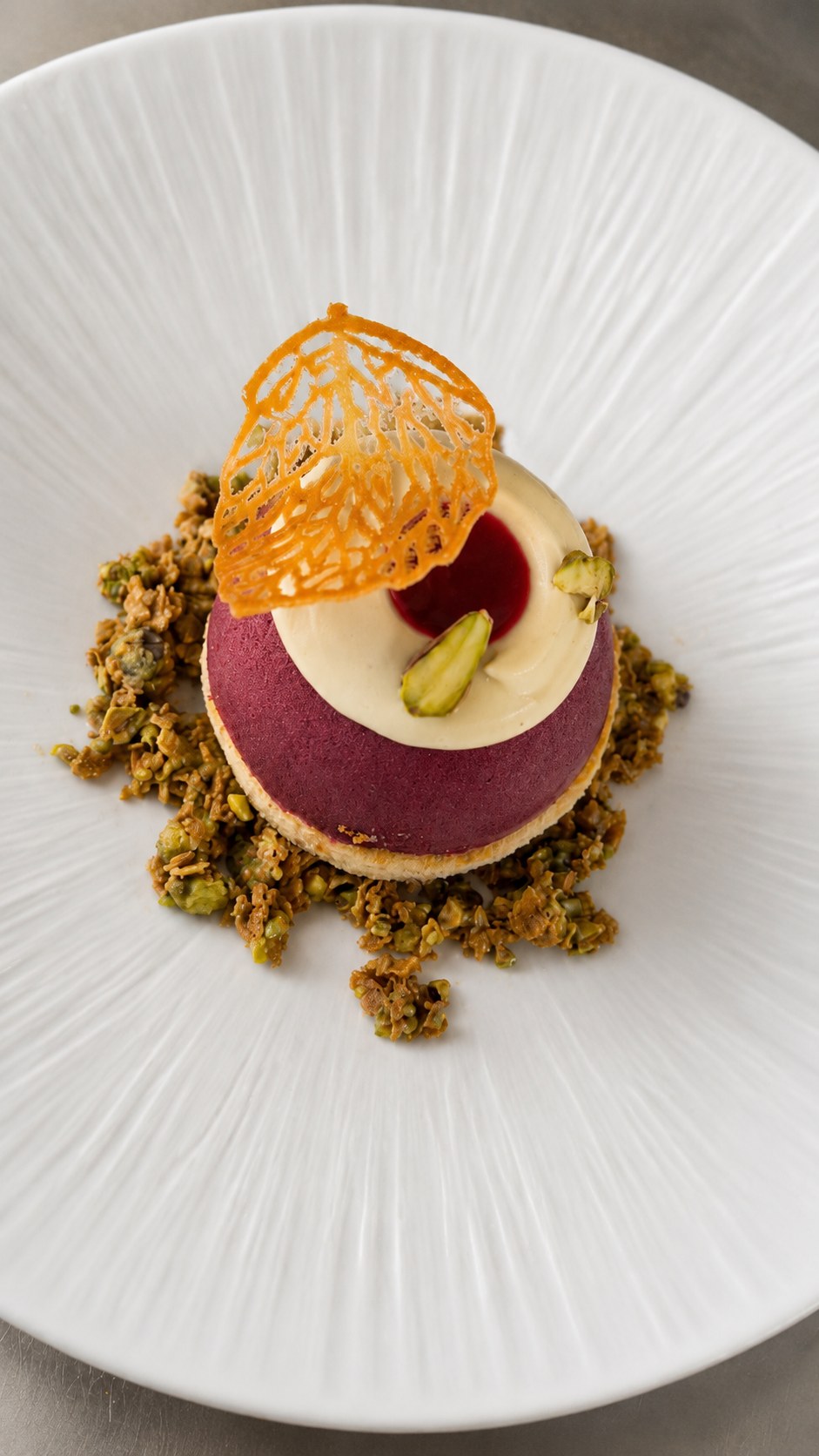 Elegant plated dessert with pistachio, berry mousse and crisp decoration.