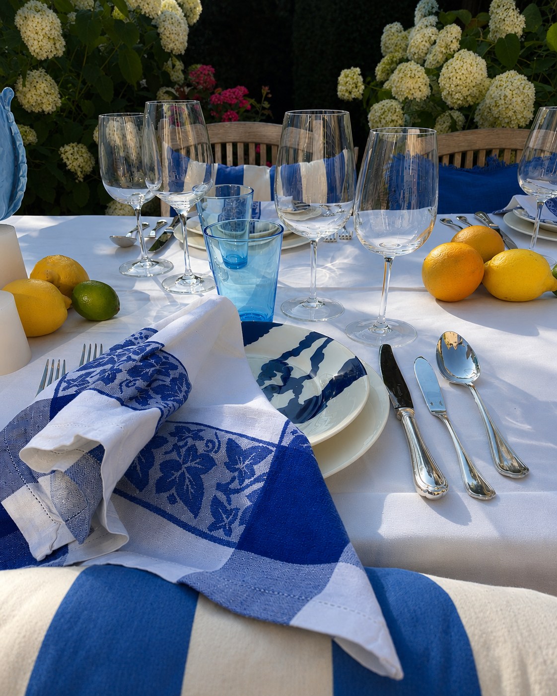 Blue and white summer table with glassware, citrus and candlelight.